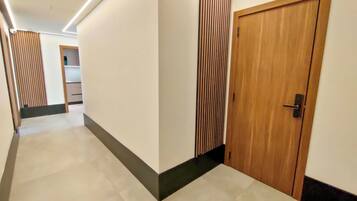 Un pasillo con una puerta de madera, un panel de pared vertical y una lámpara en el techo.