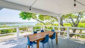 A covered outdoor dining area with a wooden table and blue chairs, overlooking a scenic view of trees and a body of water. - 4 2 wow 180 Lake Views hot tub Pickleball Tennis POA Court EV Charger Wheelchair Ramp POA Pool (Canyon Lake)