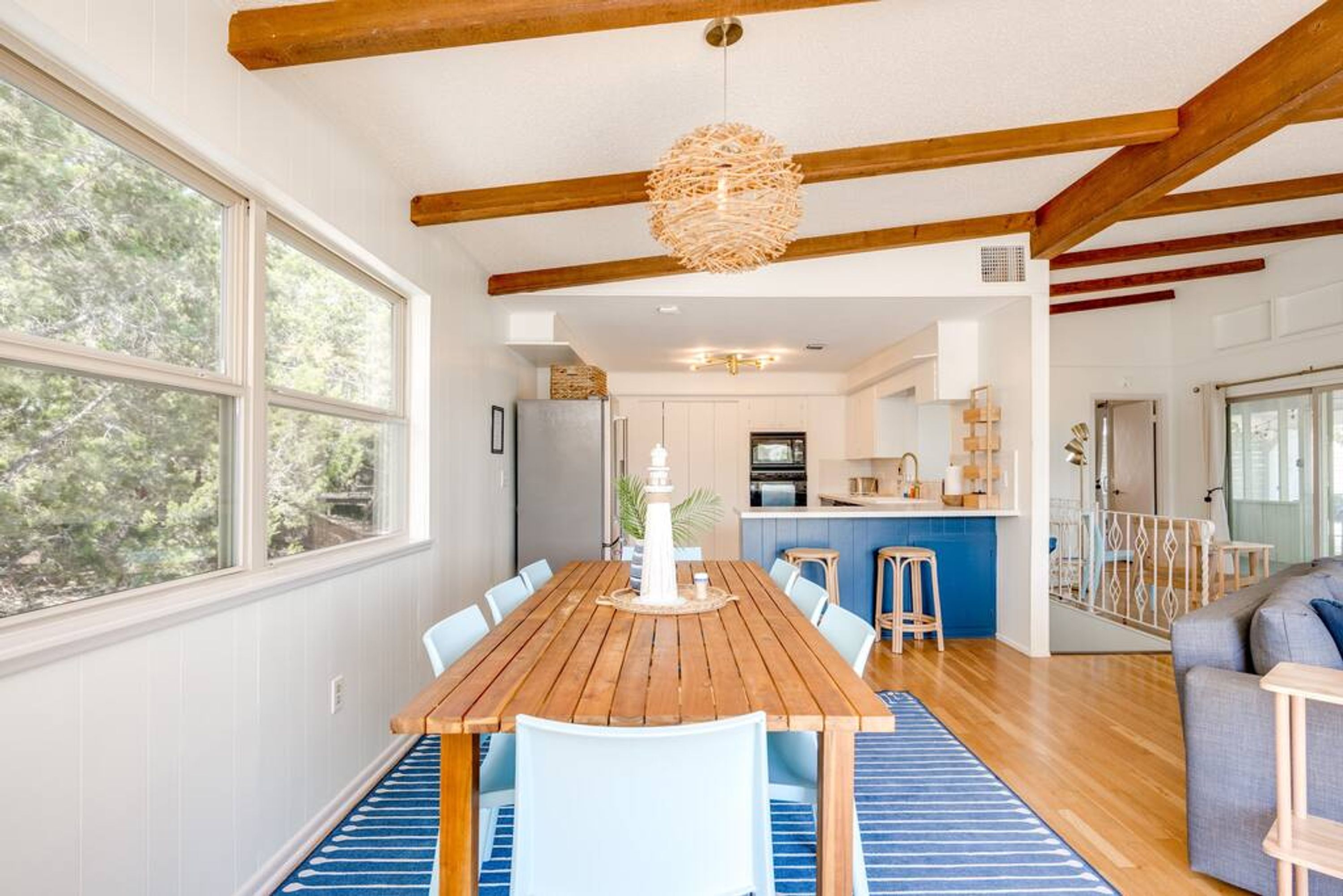 A spacious dining area with a wooden table and chairs, a hanging light fixture, and large windows offering a view of the outdoors.