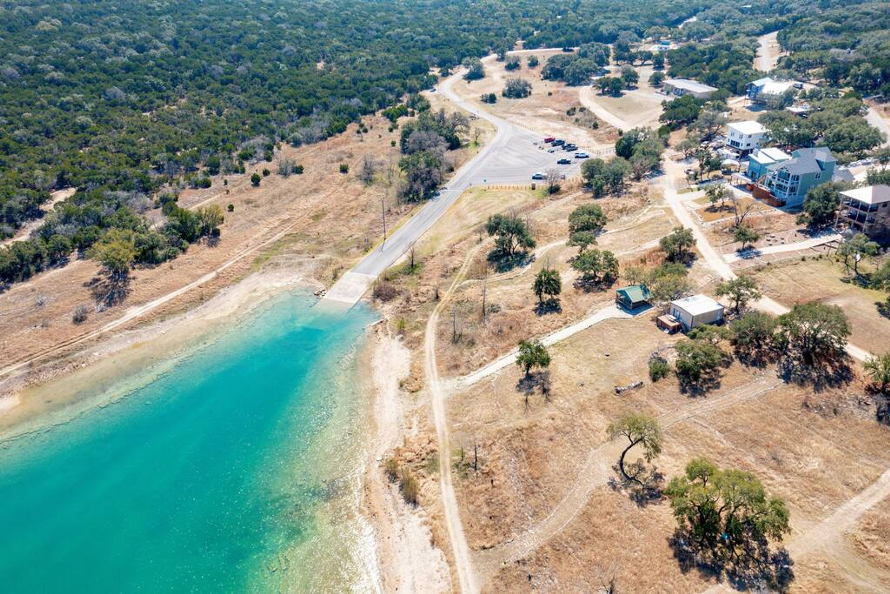 Eine Luftaufnahme eines Küstengrundstücks mit einer klaren Zufahrt zum Strand, umgeben von trockener Vegetation und Wohnhäusern.