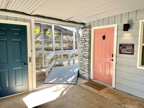 Una casa con dos puertas, una verde azulada y otra rosa, y un pilar de piedra.