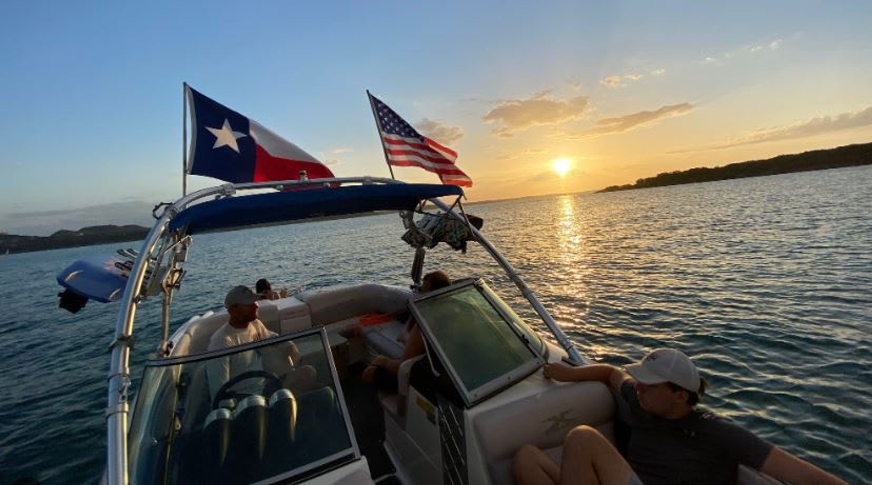 Un barco con dos banderas, cielo despejado y atardecer sobre el agua.