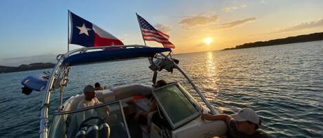 Un barco con dos banderas, cielo despejado y atardecer sobre el agua.