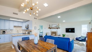 Amplia sala de estar con una mesa de comedor de madera, sofá azul y una cocina moderna con armarios blancos.