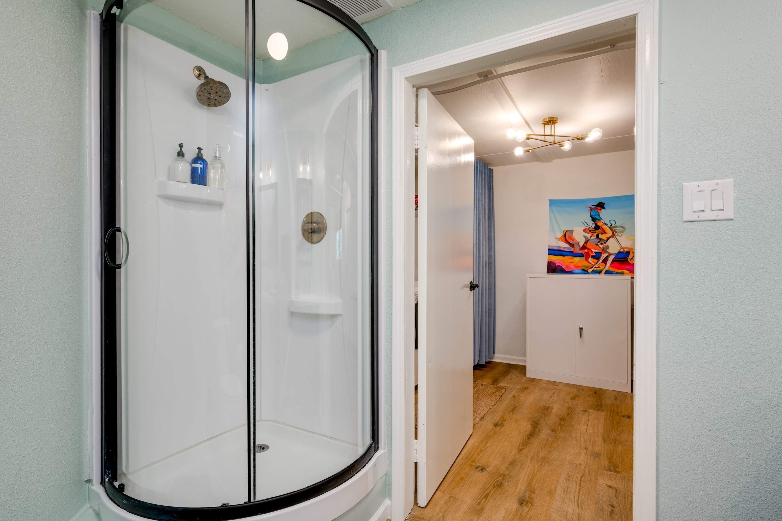 A modern bathroom with a glass shower enclosure, a white sink, and a shelf with toiletries.
