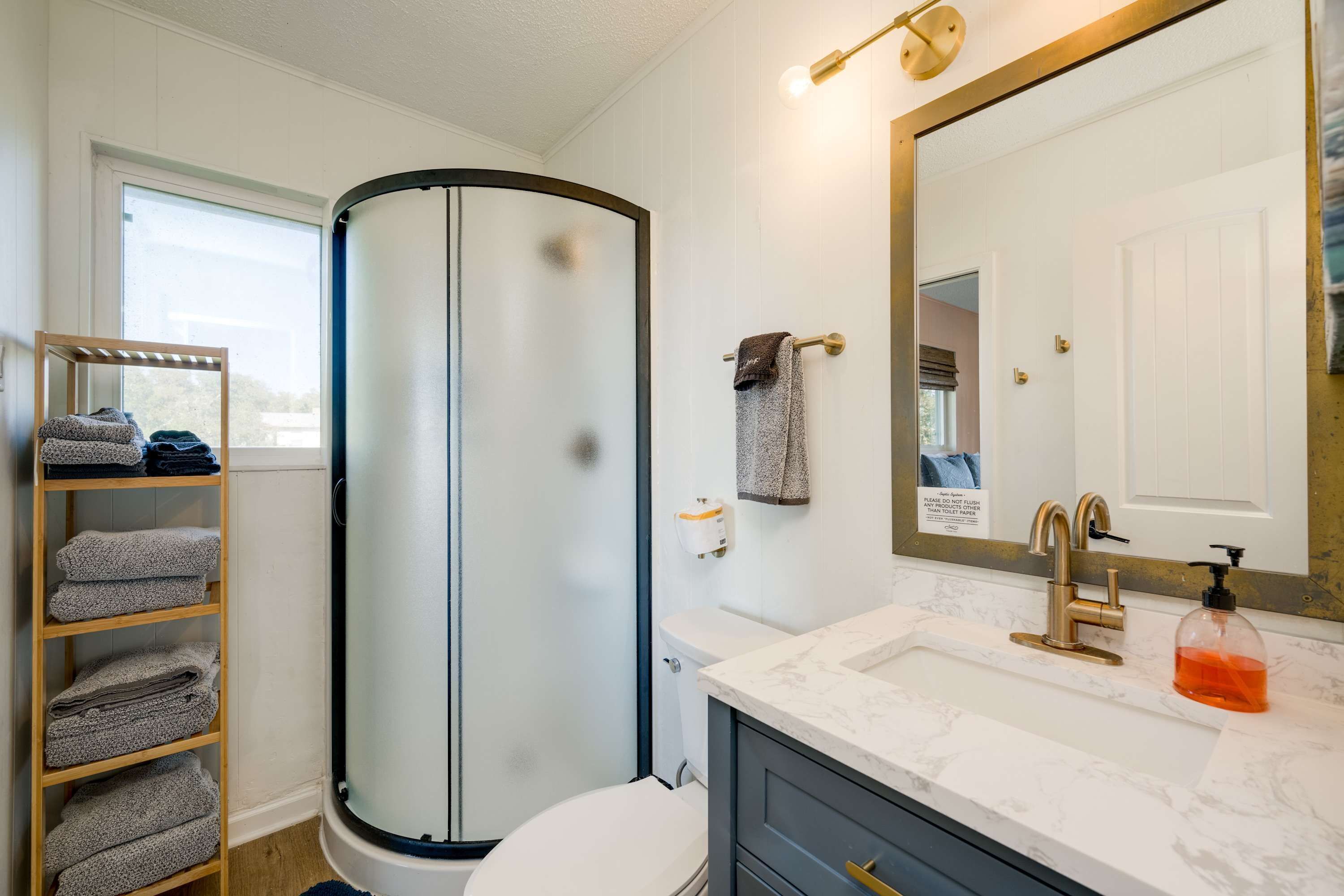 Un baño con cabina de ducha de vidrio, inodoro, lavabo con encimera de mármol, toallero y un espejo grande.