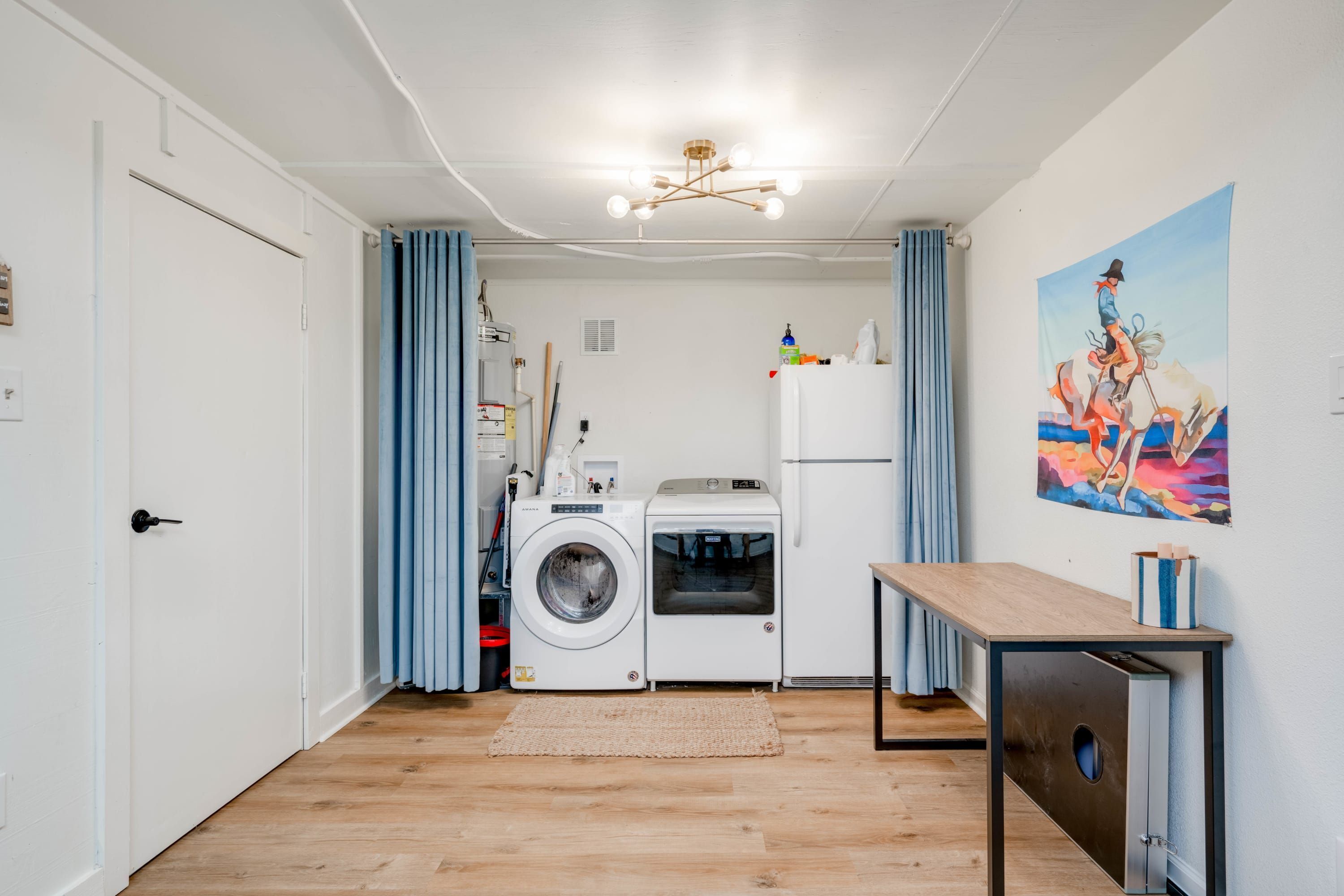 A compact living space with a washing machine, a small table, and a painting on the wall.