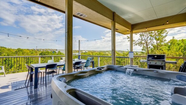 Un bain à remous sur une terrasse en bois, avec des sièges d’extérieur et une vue sur une zone boisée.