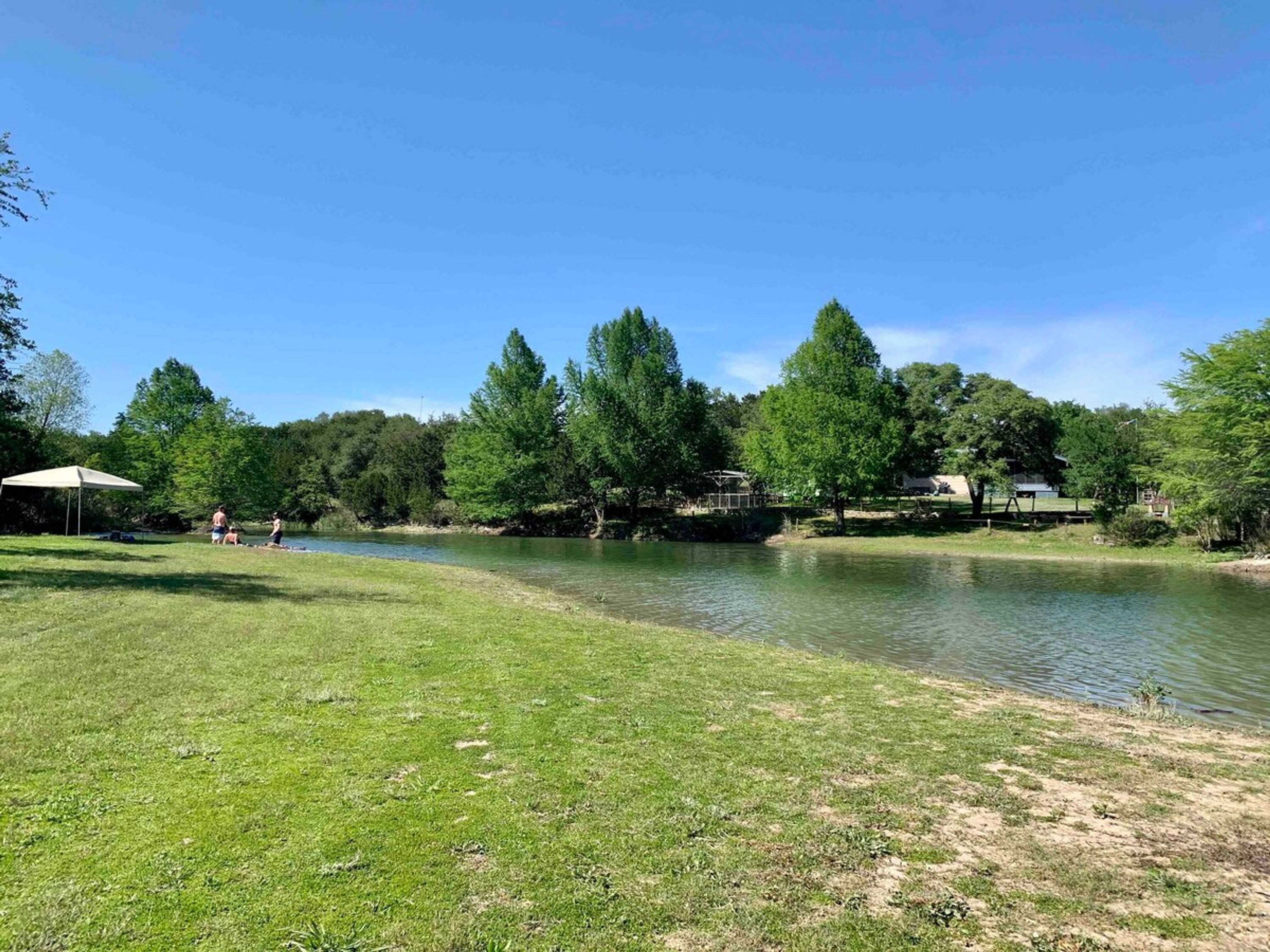 A grassy area with a lake, trees, and a pavilion.