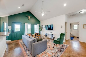 Un salón amplio con una pared de acento verde, ventilador de techo, un televisor de pantalla plana grande y una distribución de asientos cómoda.