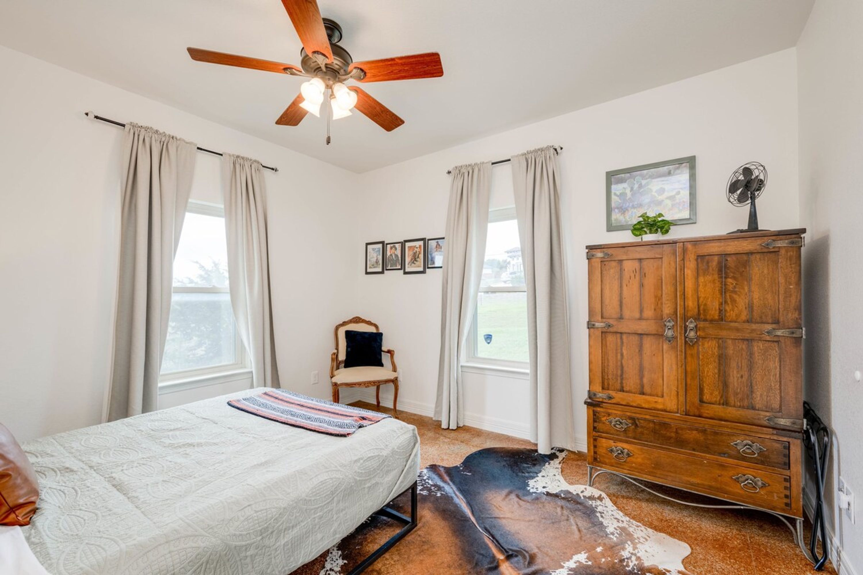 A bedroom with a bed, a wooden dresser, a ceiling fan, and a cowhide rug.