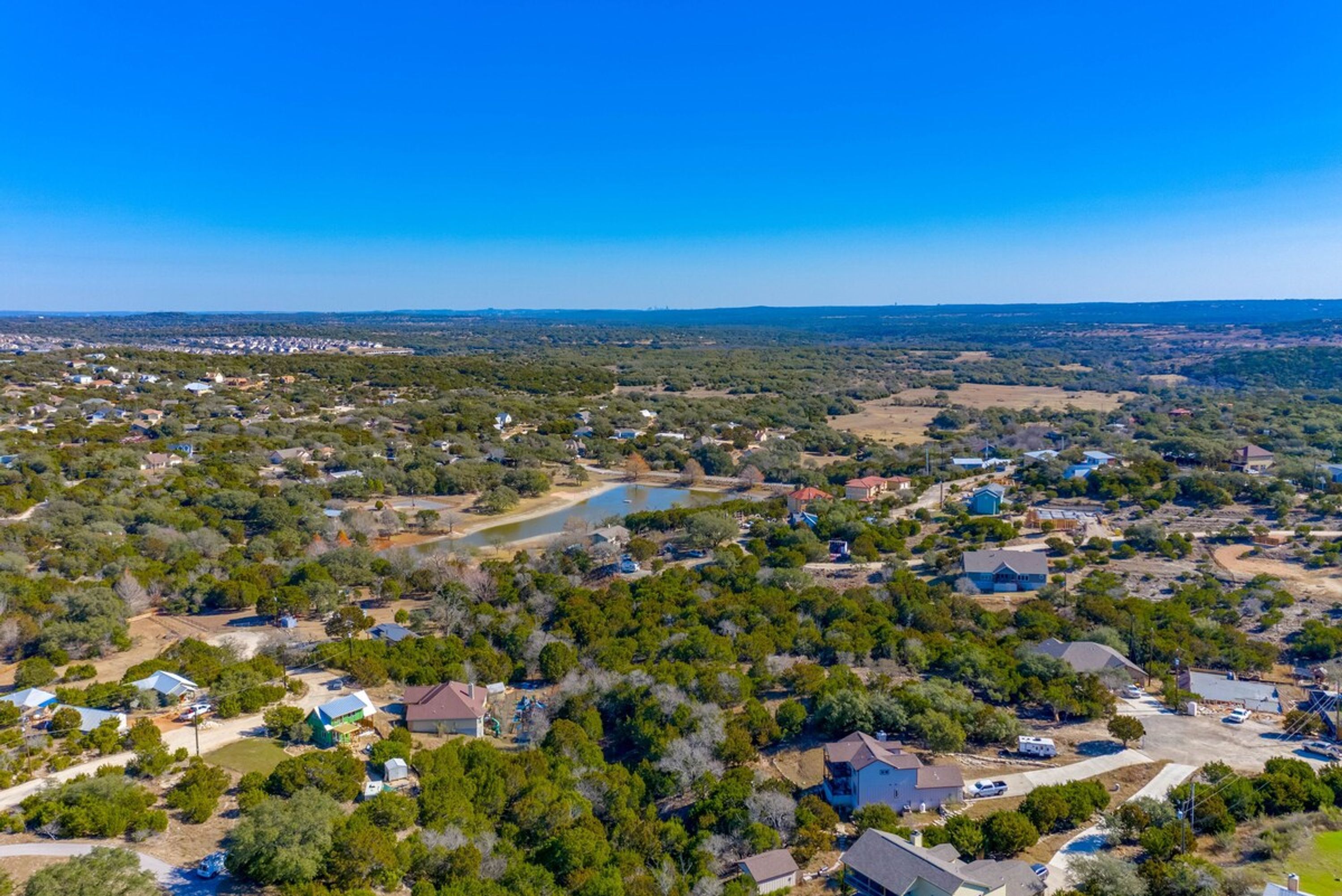 An aerial view of a residential area with houses, a lake, and surrounding greenery.