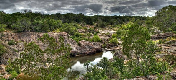 A natural landscape with a rocky terrain and a small water body surrounded by dense greenery.