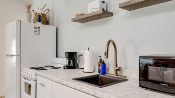Una cocina con un refrigerador blanco, una cafetera, un lavamanos y un microondas.