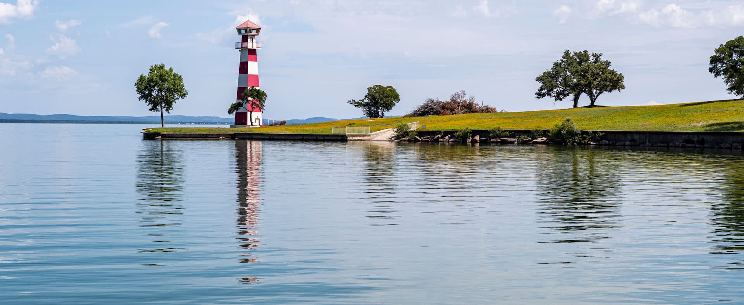 A lighthouse on a grassy island with calm water reflecting its structure.