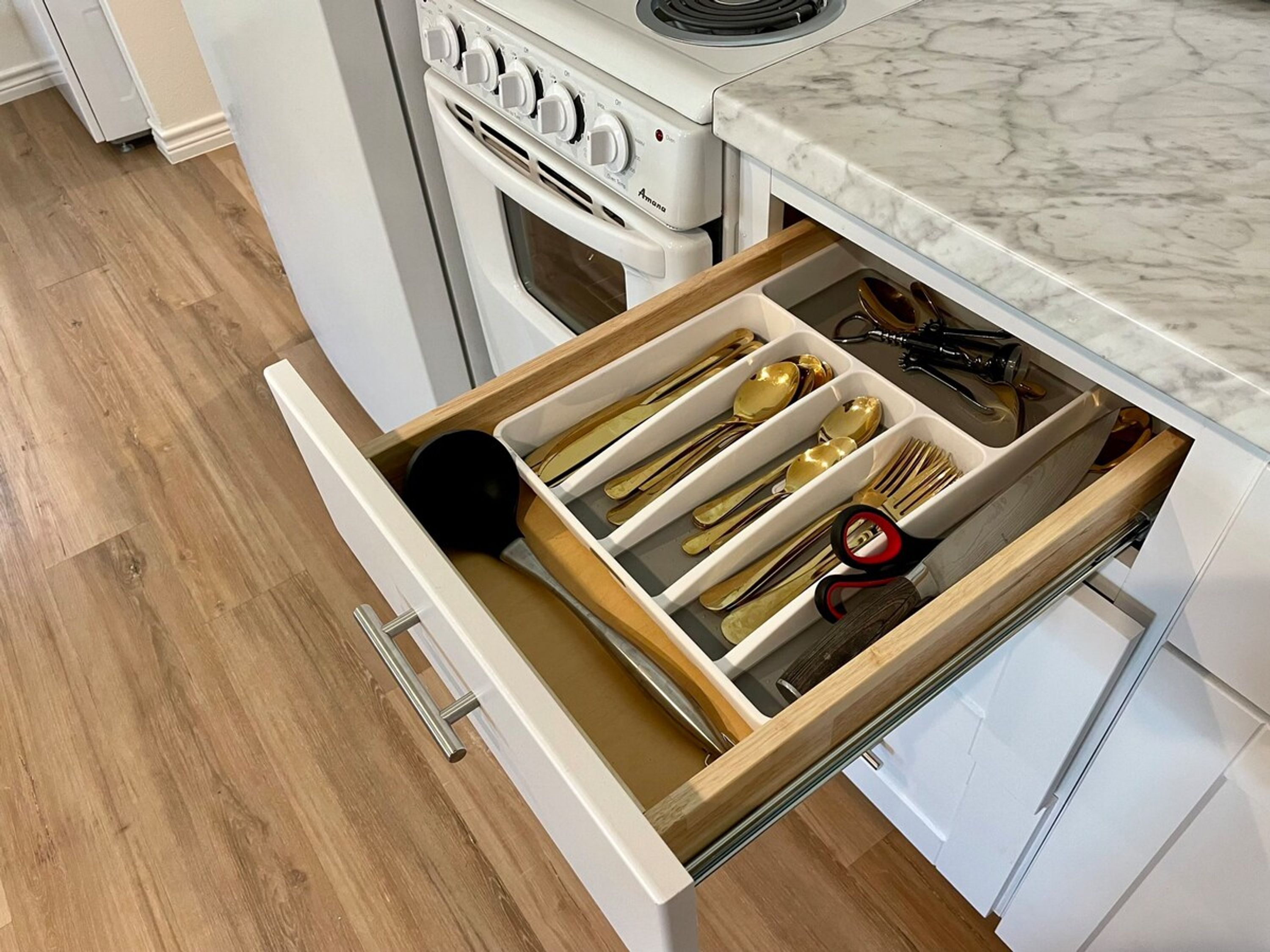 A kitchen with a white stove, a drawer with utensils, and a marble countertop.