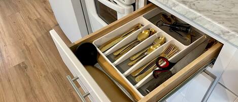 A kitchen with a white stove, a drawer with utensils, and a marble countertop.