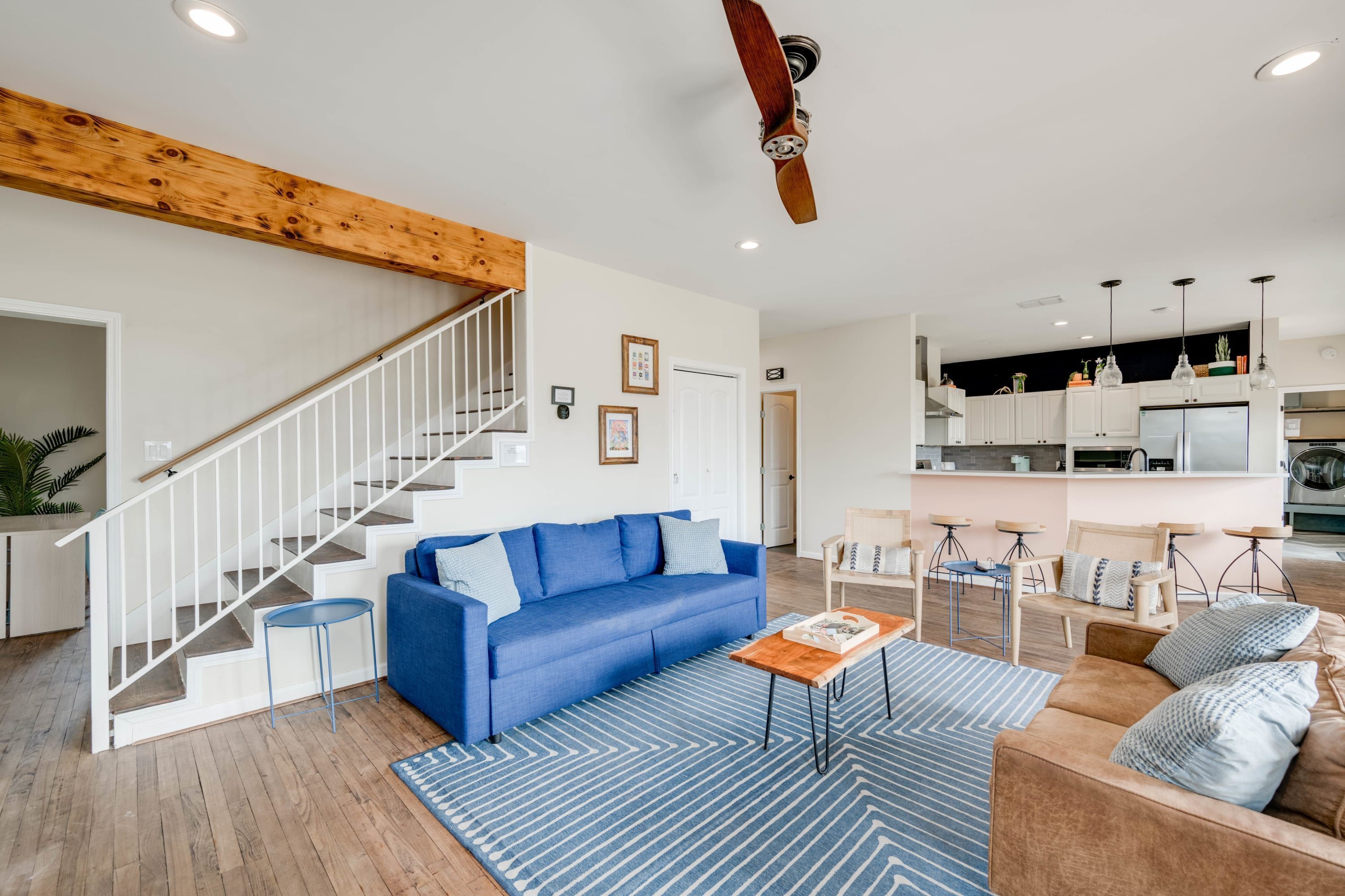 Un salon moderne avec un canapé bleu, une table basse en bois et un escalier doté de rampes blanches.