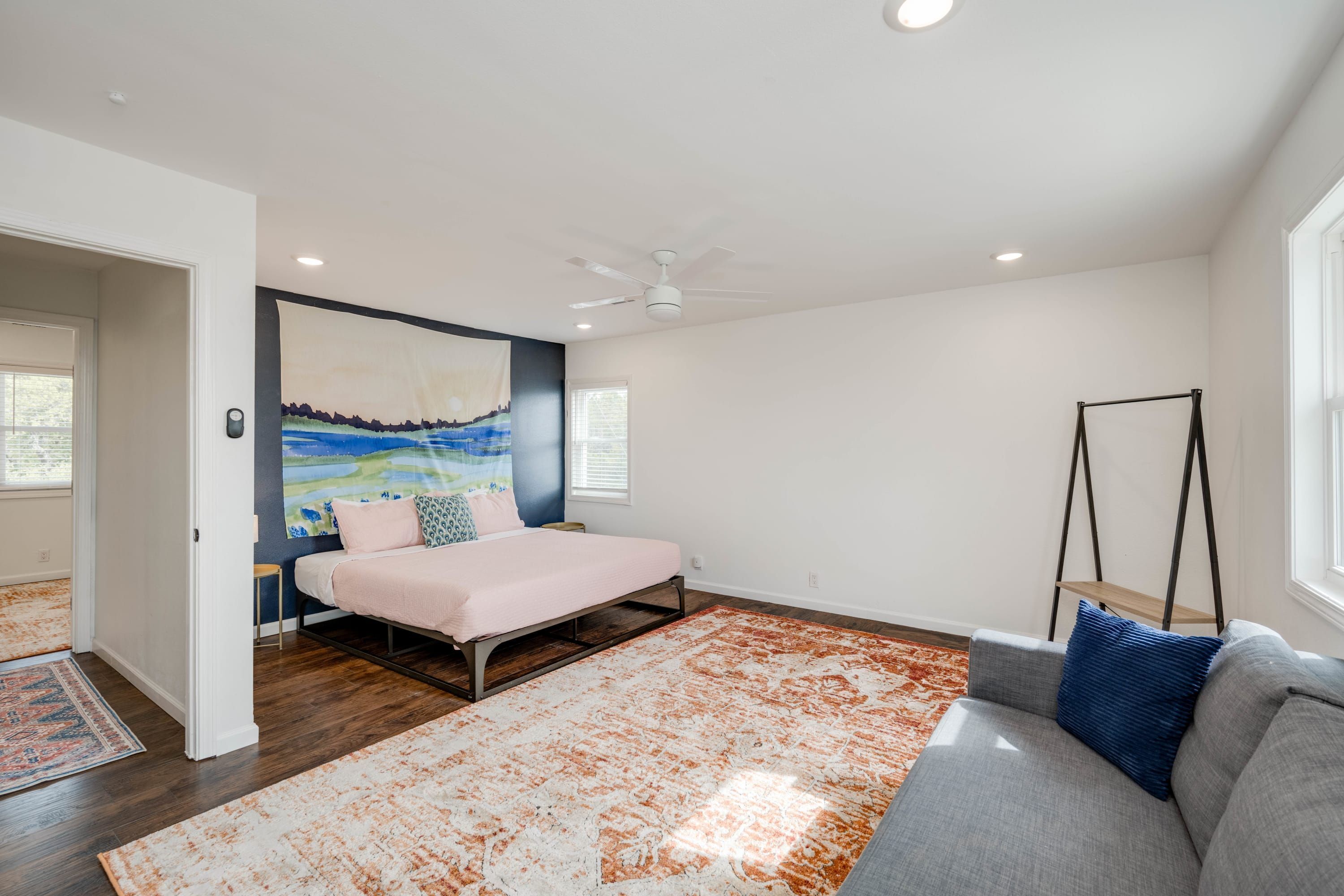 Una camera da letto con un letto, un divano grigio, una ventola a soffitto e un'ampia finestra.