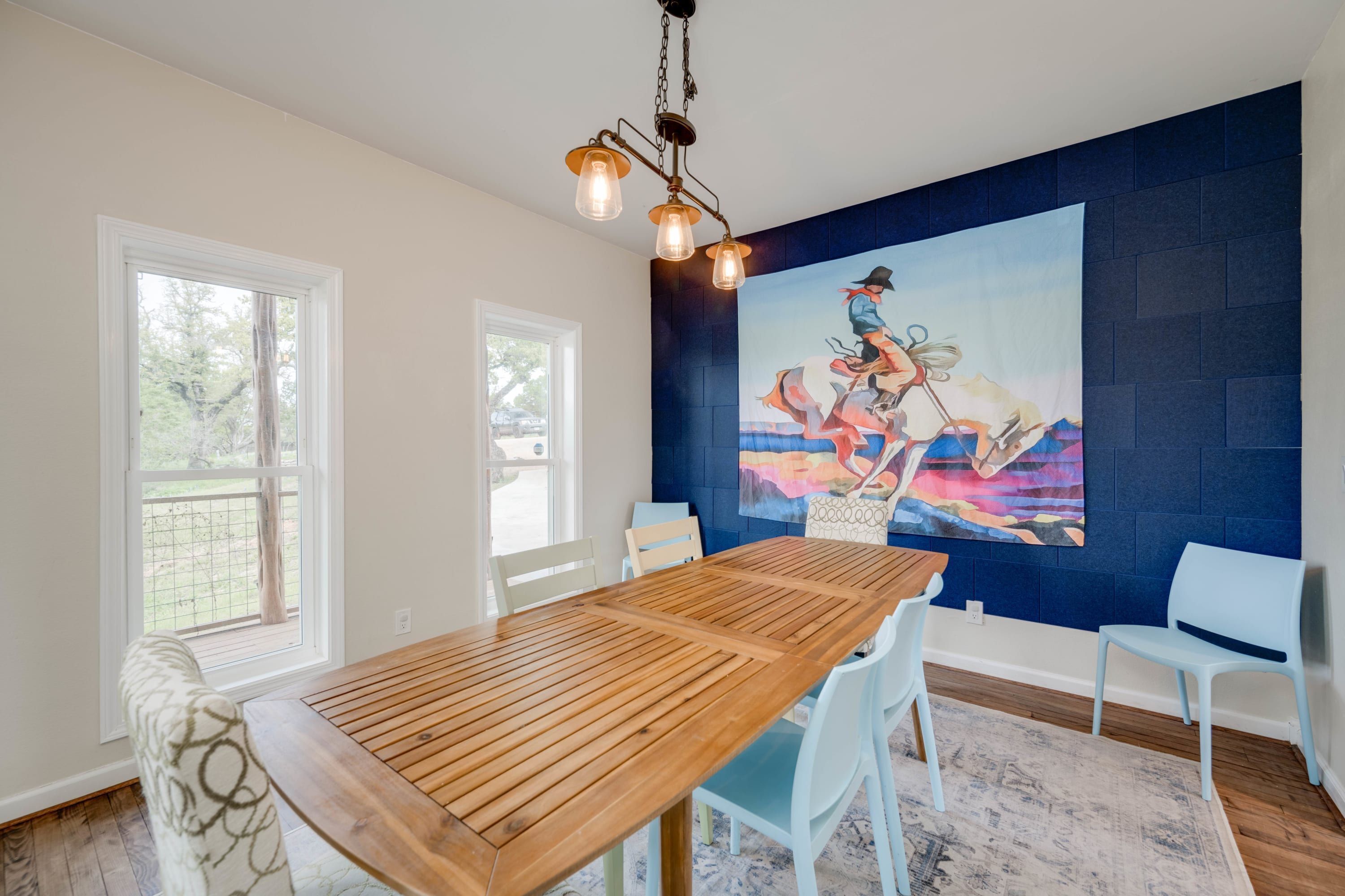 Un coin repas avec une table en bois, des chaises blanches, un mur d’accent bleu et un tableau.