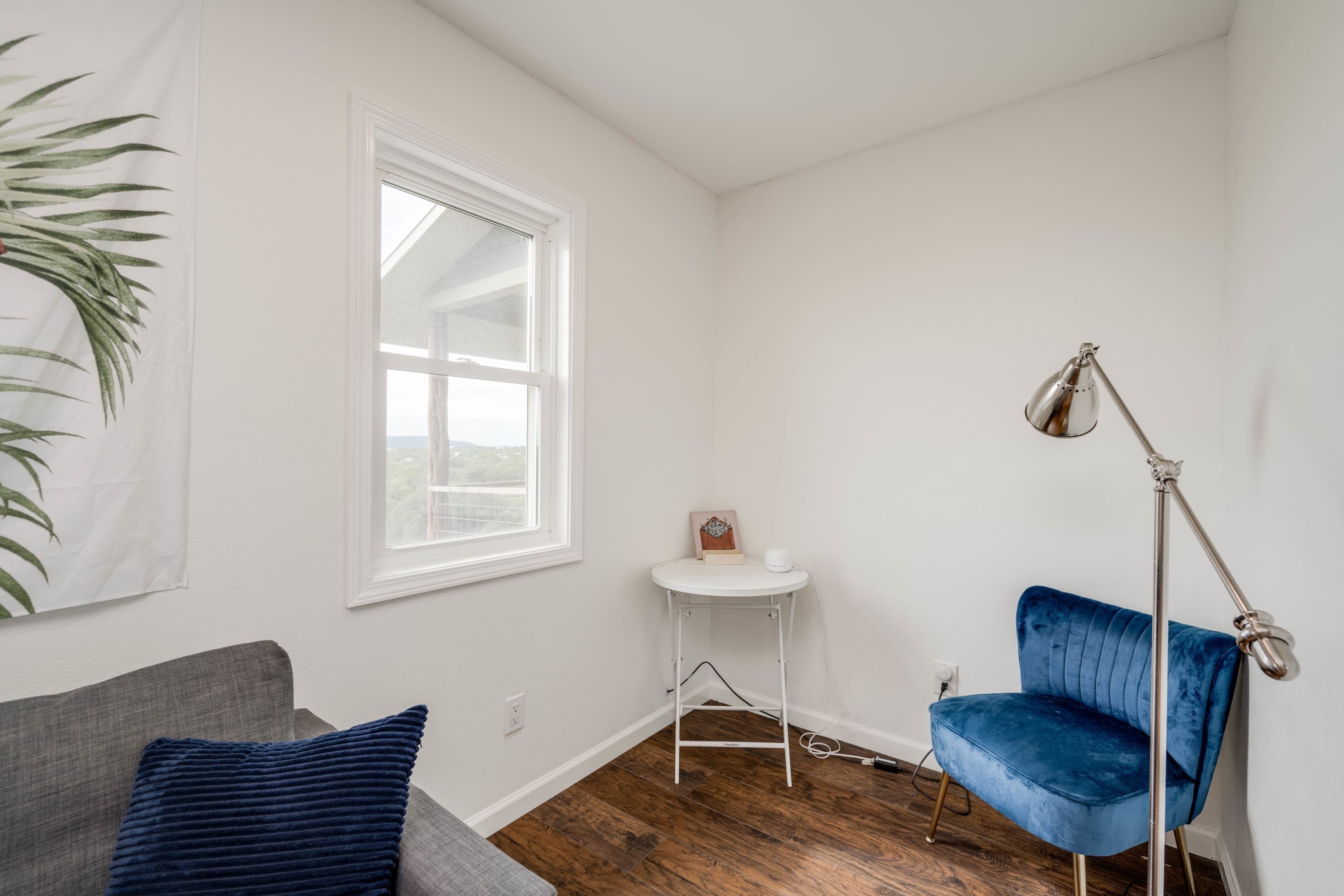 Una habitación con un sofá gris, una silla azul, una mesa blanca y una lámpara de pie.