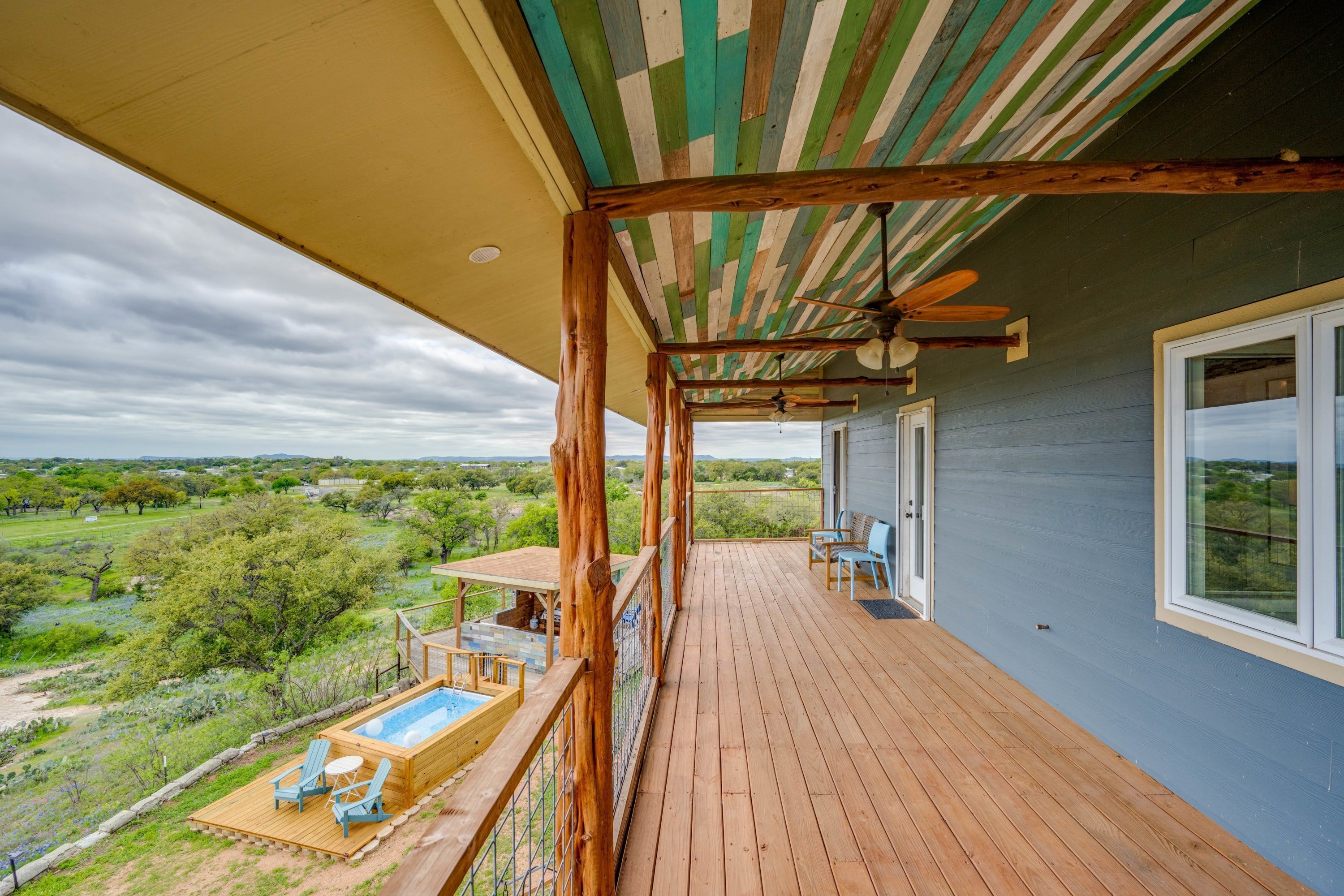 A wooden deck with a pool, chairs, and a table overlooking a scenic landscape.