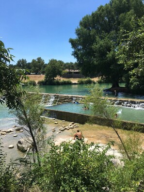 Un plan d’eau naturel agrémenté d’une petite cascade, entouré d’arbres et surplombé d’un ciel dégagé.