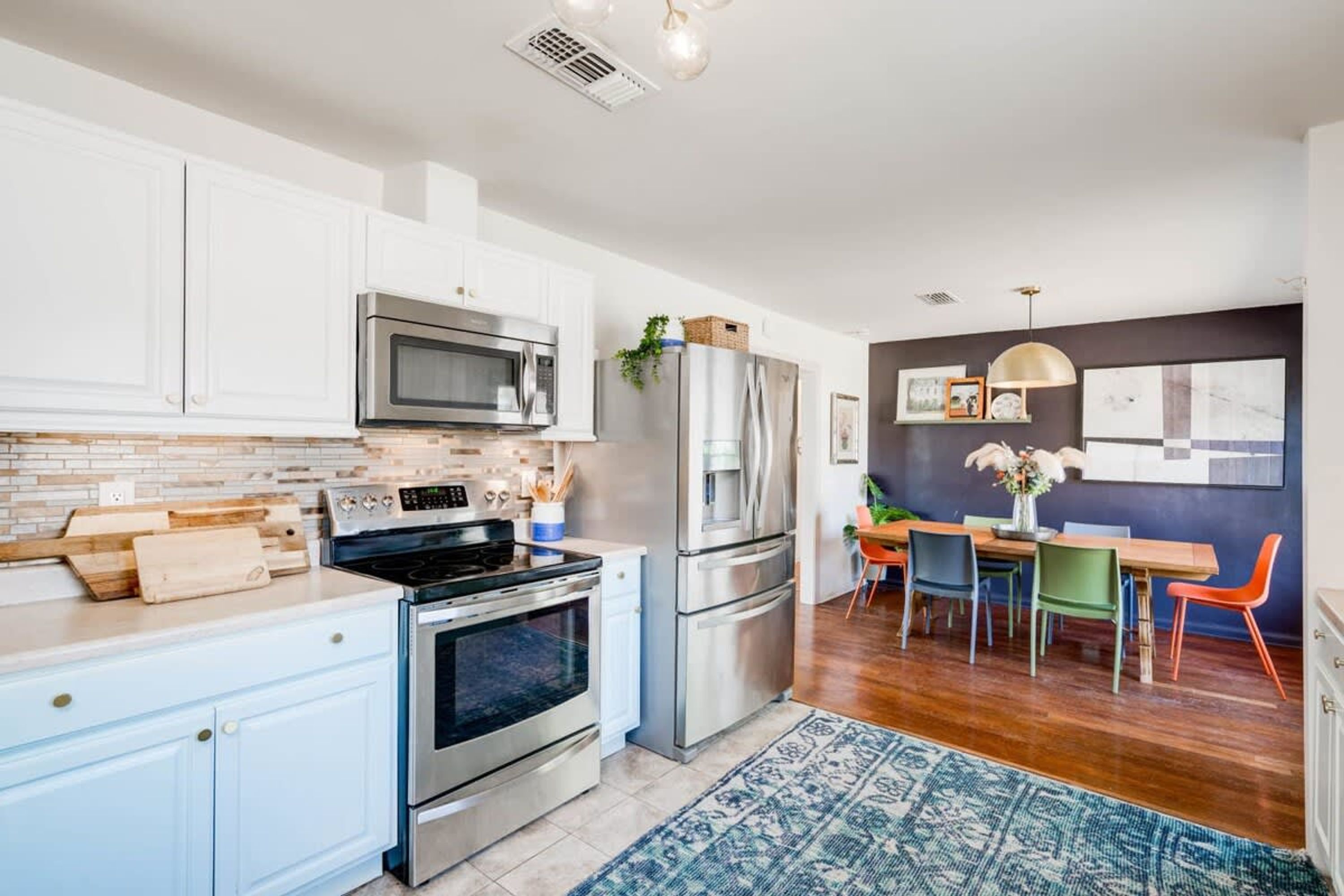 A modern kitchen with white cabinets, stainless steel appliances, and a dining area with a wooden table and colorful chairs.