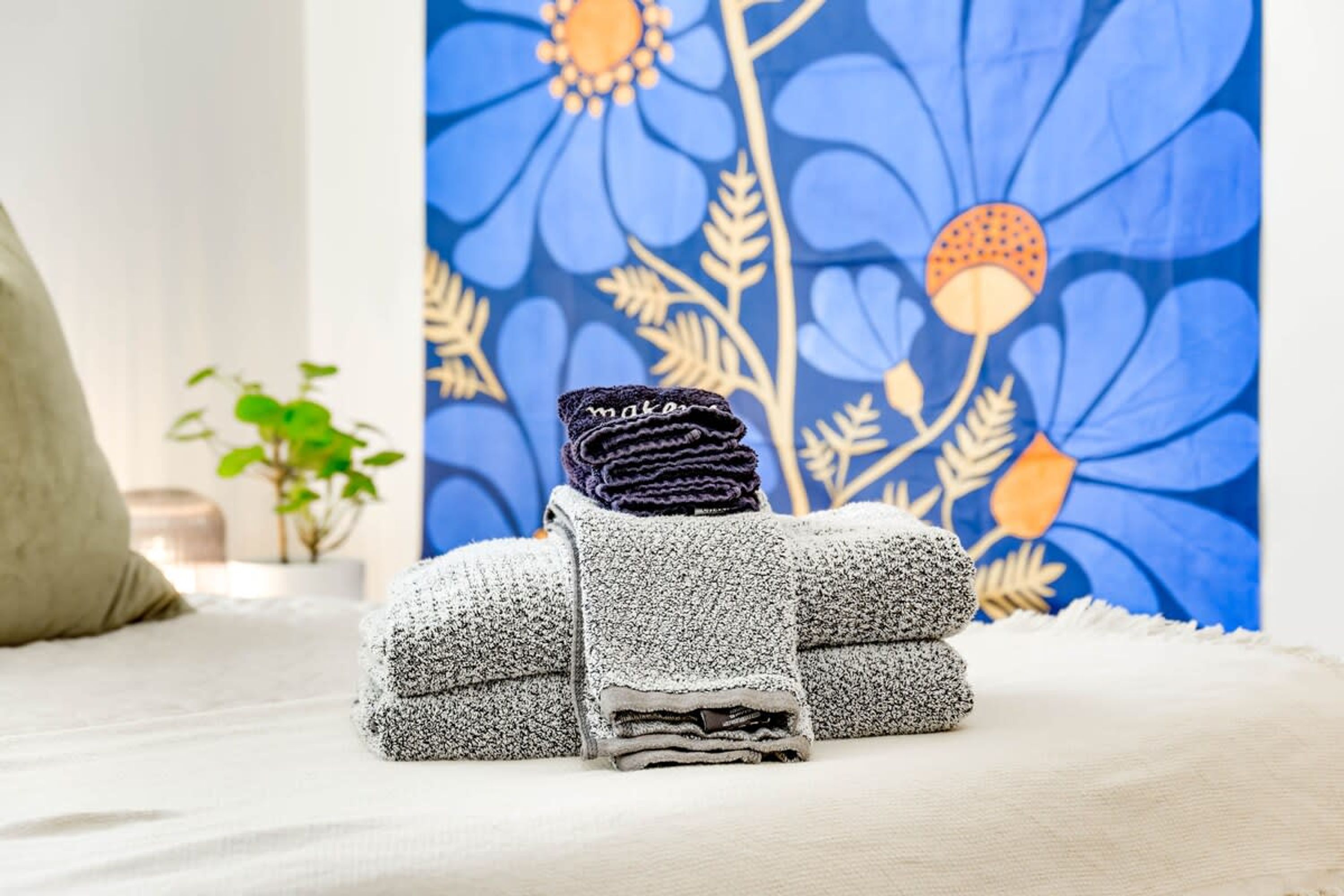 Toalha dobrada com cuidado, com etiqueta, sobre a cama, com papel de parede floral ao fundo.