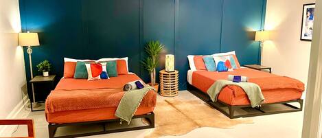 A modern bedroom with two beds, each with a unique headboard, a small round table, and a potted plant.