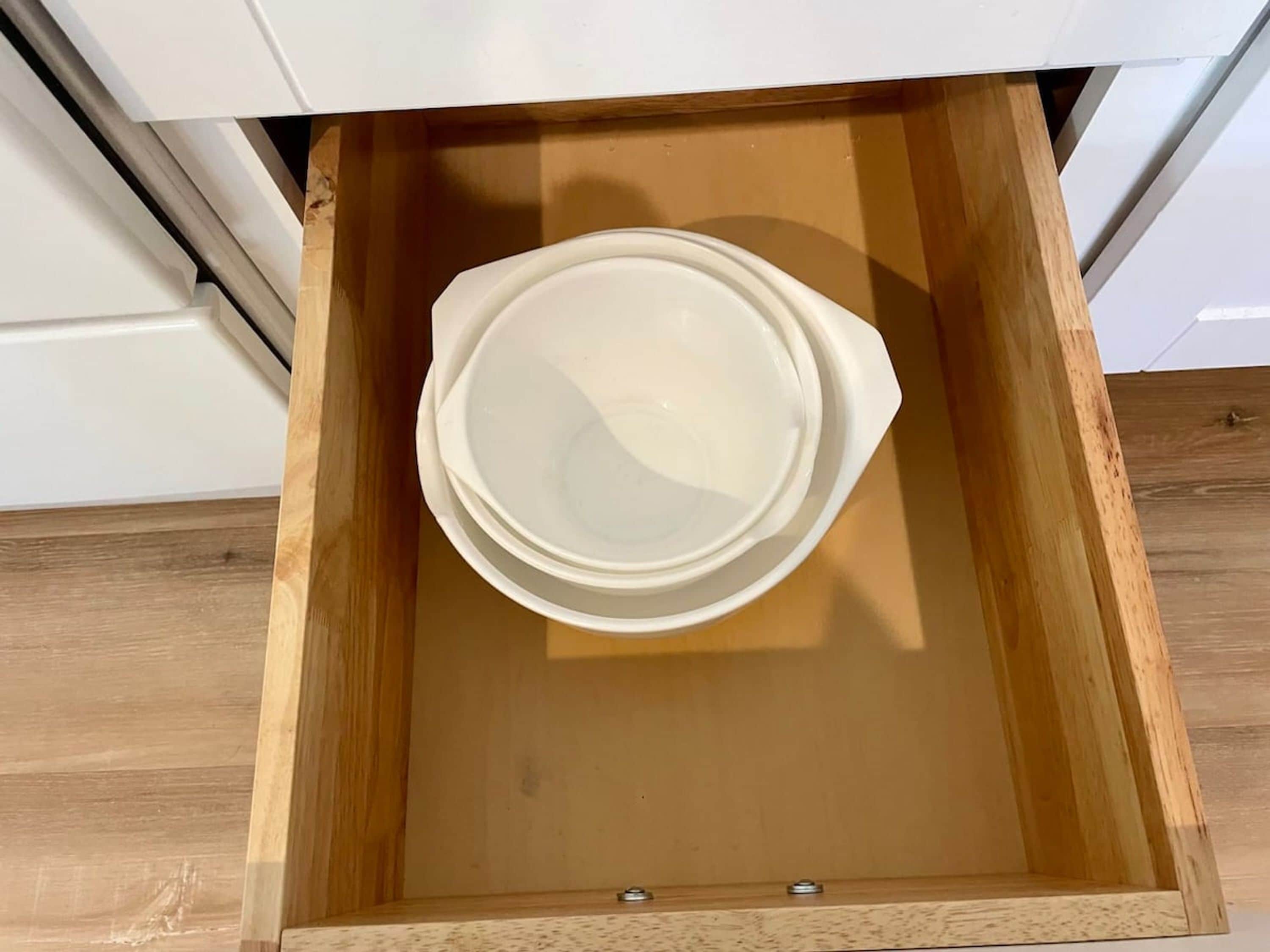 A wooden drawer with a white interior and a white exterior, containing a stack of white bowls.