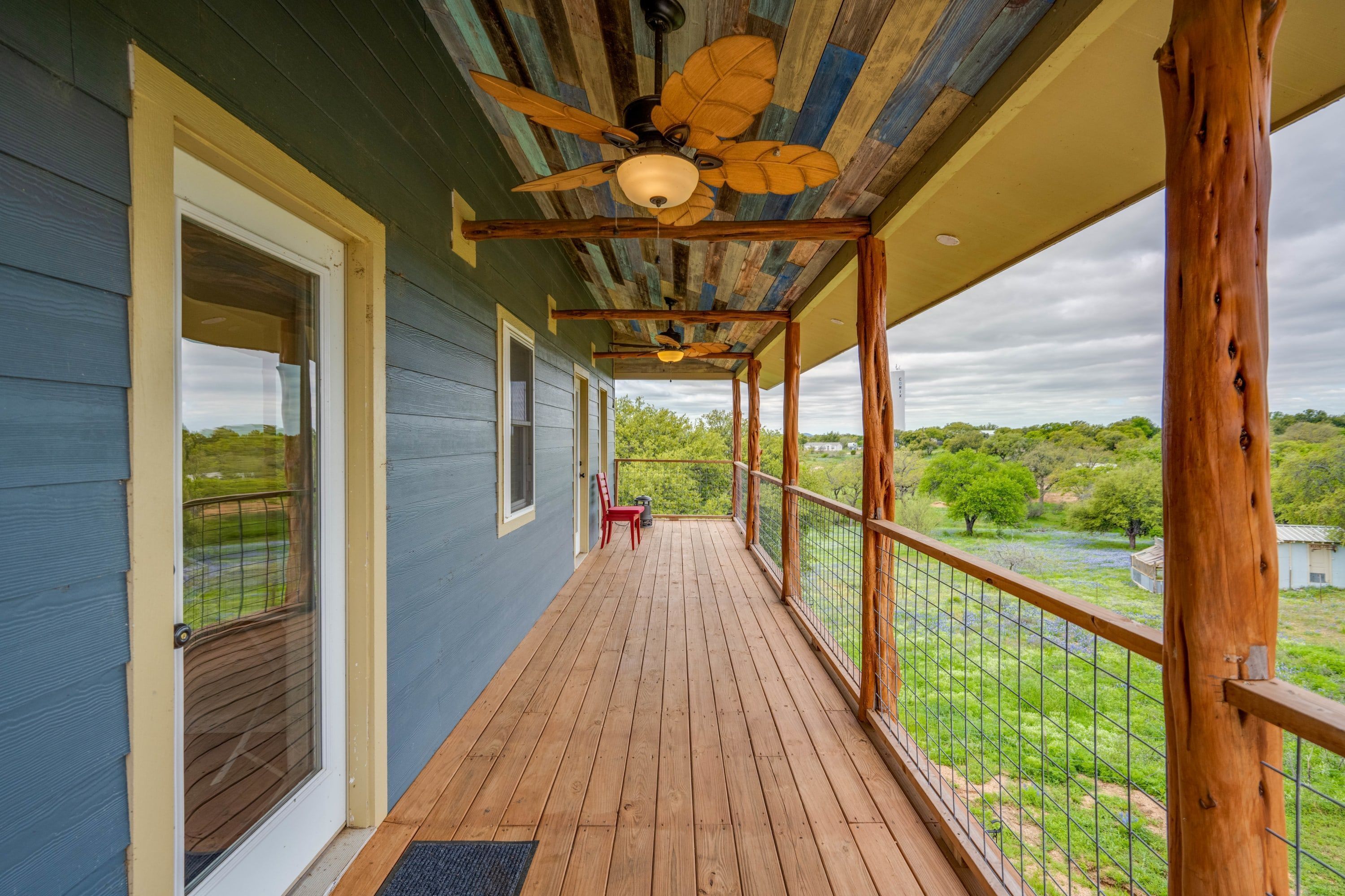 Une véranda couverte avec un plancher en bois, un ventilateur de plafond et une vue sur un paysage verdoyant.