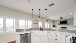 Una cocina moderna con muebles blancos, lavavajillas y un ventanal grande.