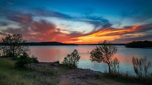 Solnedgang over en rolig sø med træer i forgrunden.