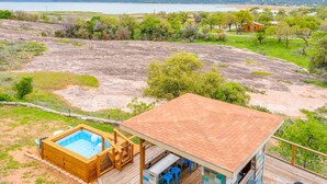 Una terraza de madera con un jacuzzi, un espacio de estar cubierto y vistas a un lago y un paisaje lejano.