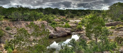 A natural landscape with a rocky terrain, a small water body, and dense greenery.