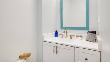 A bathroom with a white sink, gold faucets, a blue soap dispenser, and a small potted plant.