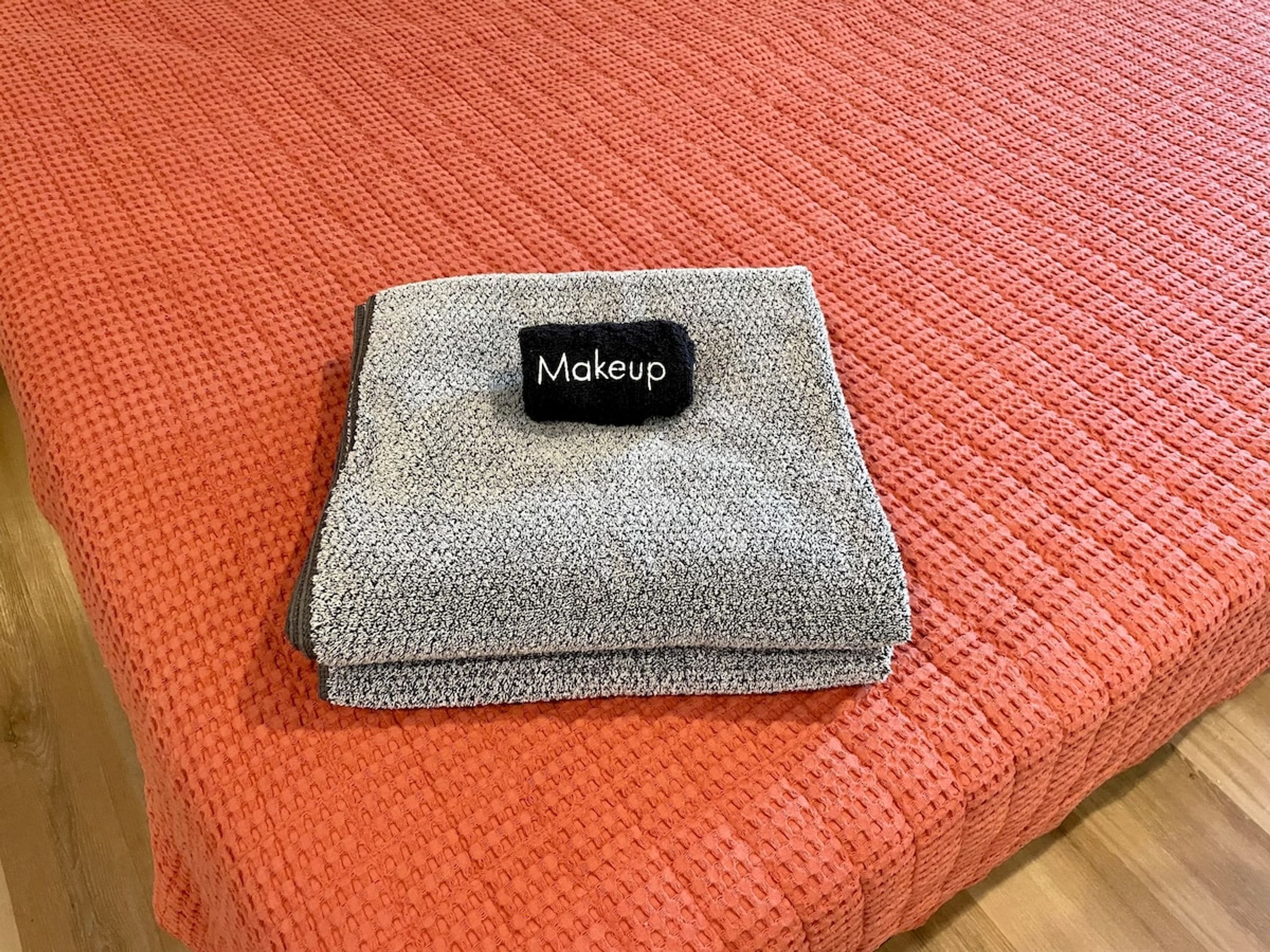 A neatly folded grey blanket with a black tag labeled "Makeup" on a red textured ottoman.