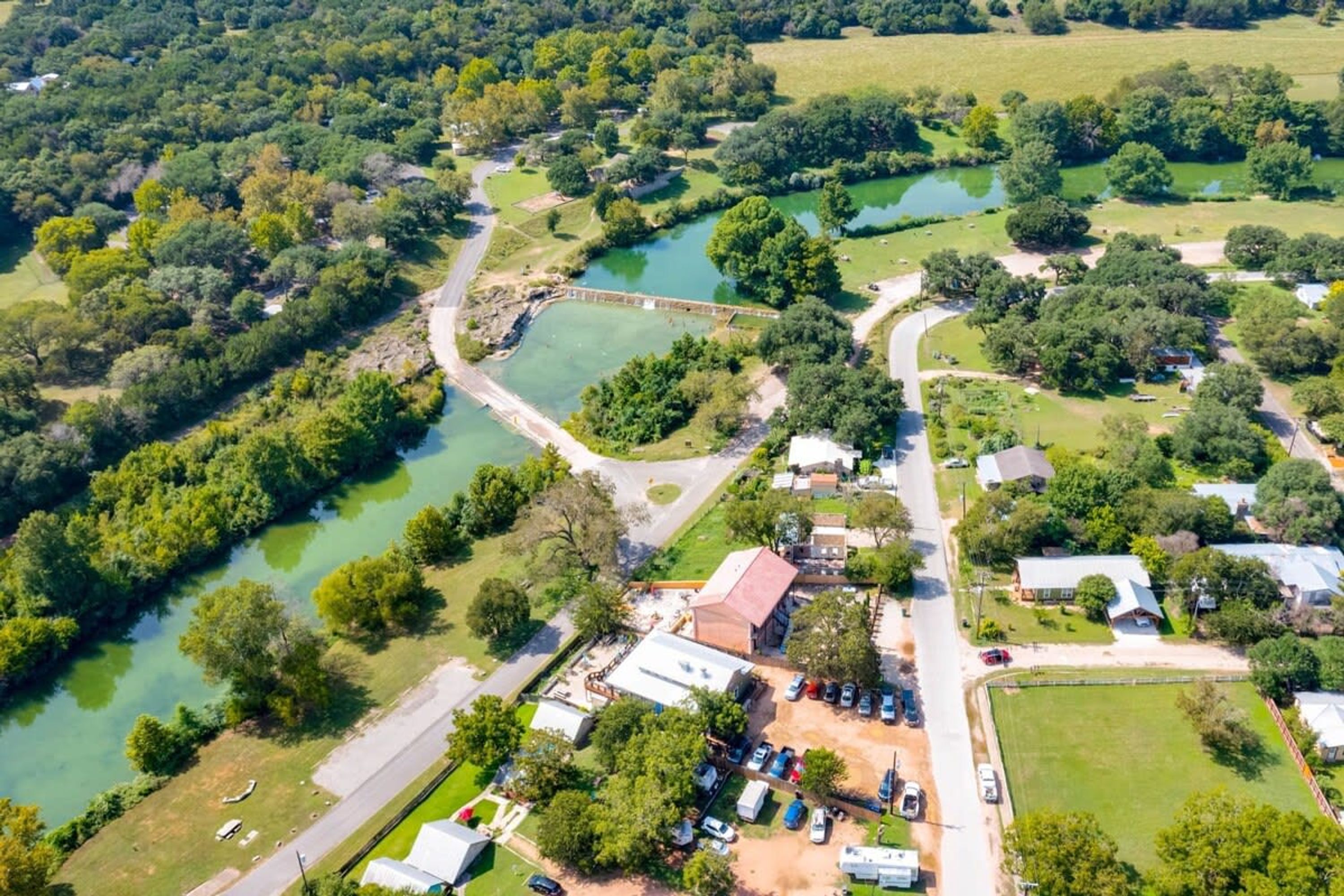 An aerial view of a residential area with a river, a bridge, and houses with parked cars.