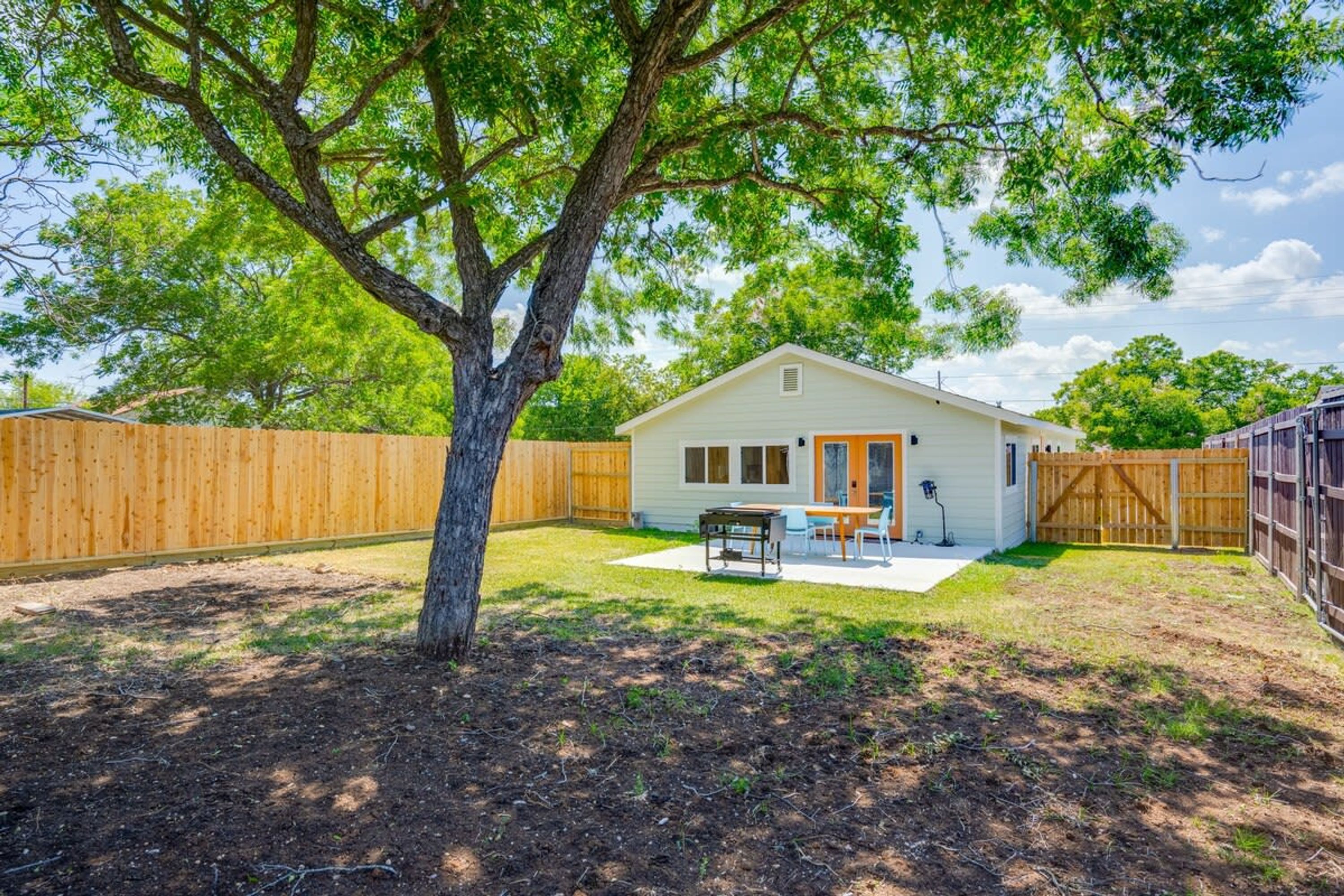 A single-story house with a fenced backyard, a patio with a table and chairs, and a wooden fence.