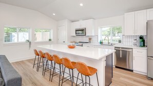 Una cocina moderna con armarios blancos, una isla grande con taburetes de bar, electrodomésticos de acero inoxidable y lavavajillas.