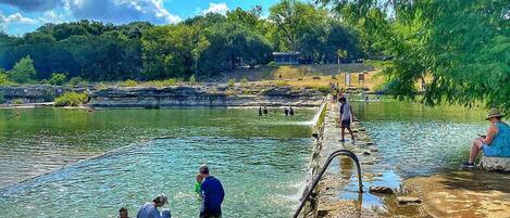 A natural water body with people engaging in water activities, surrounded by trees and a rocky landscape.