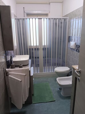 Ein modernes Badezimmer mit Badewanne, Toilette und Bidet. Es gibt eine grüne Matte, einen Handtuchhalter und eine dekorative Fliesenrückwand.