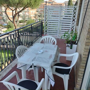 Ein Balkon mit Tisch und Stühlen, einem weißen Zaun und Blick auf Gebäude und Bäume.