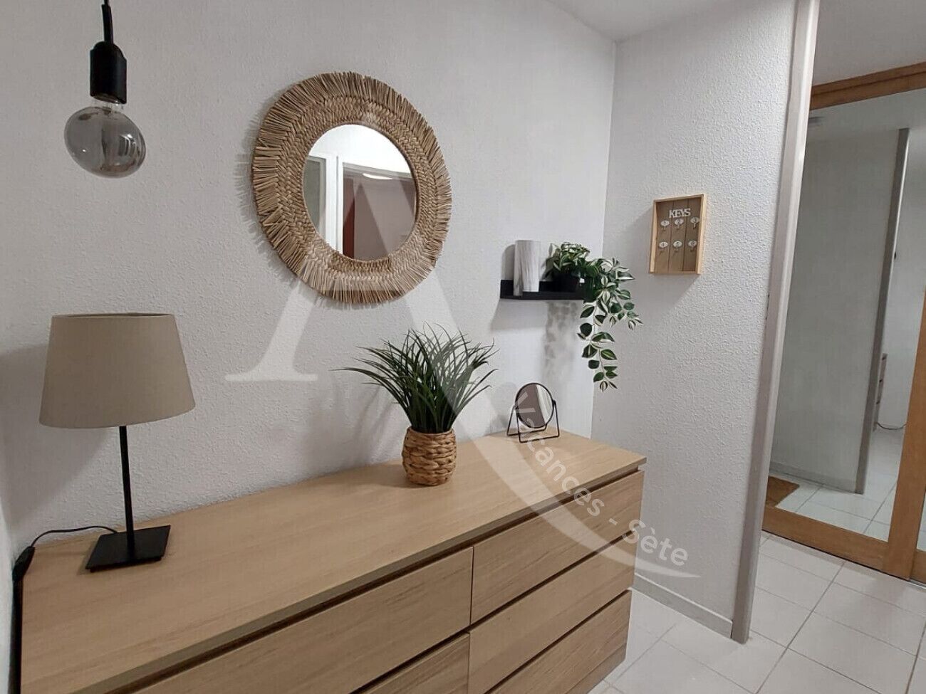 A modern bathroom with a wooden vanity, a round mirror, a potted plant, and a towel rack.