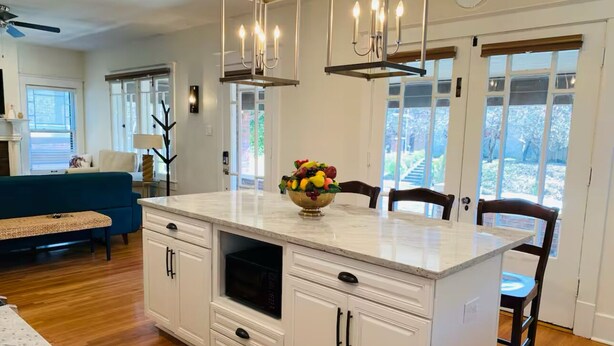Una cocina con una isla central, muebles blancos y un cuenco de fruta en la encimera.