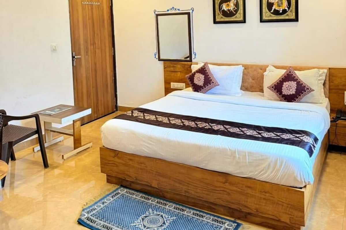 A hotel room with a wooden bed, a desk, a chair, a blue patterned rug, and a ceiling with decorative lighting.