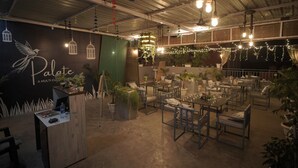 A restaurant with a rustic interior, featuring hanging light bulbs, string lights, and potted plants. - Hotel Haridas Haveli Udaipur (Udaipur)