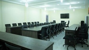 A conference room with a long table and multiple chairs, a flat-screen TV mounted on the wall, and a door in the background. - Henry George Hotels (Ilorin)
