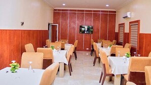 A dining area with tables and chairs, a television mounted on the wall, and a wooden panel design on the walls. - Henry George Hotels (Ilorin)